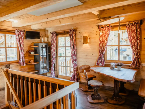 Gemütliches Baumhaus-Interieur mit Holzmöbeln, großen Fenstern und roten Vorhängen im Schwarzwald.