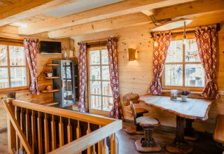 Interior de alojamiento glamping de madera, con grandes ventanas, cortinas rojas y muebles rústicos en Selva Negra.