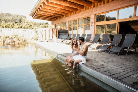 Couple enjoys drinks by the outdoor pool and lounge chairs at s'Baumhaus Dörfle glamping, Black Forest.