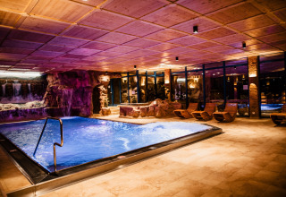 Zona spa interna con piscina illuminata, cascate e sdraio di legno a s'Baumhaus Dörfle - Boomhutten Zwarte Woud glamping.