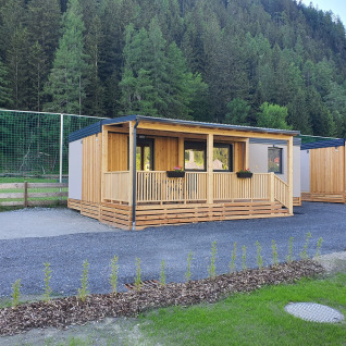 Moderne glamping hytter med træterrasse hos HochOBEN - Stacaravans Oostenrijk, omgivet af skov og bjerge.