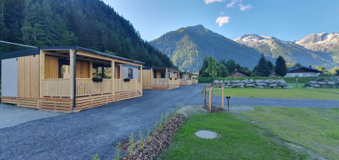 Des mobil-homes de glamping HochOBEN en Autriche, entourés de montagnes et forêt sous un ciel bleu clair.