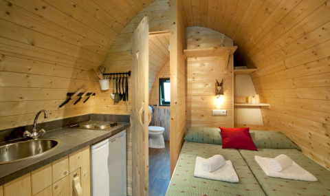 Indvendig udsigt over Nature Resort Natterer See Woodlodges Tirol med træmøbler, seng og lille køkken.