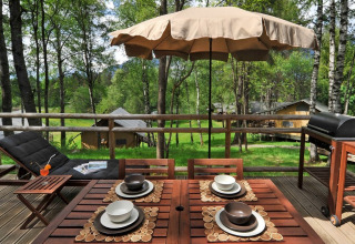 Holzterrasse mit Esstisch, Sonnenschirm und Grill beim Glamping im Nature Resort Natterer See - Woodlodges Tirol.