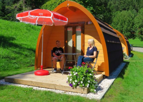 Glamping på Camping Putterersee med hyggelige pods i Østrig, to personer sidder ved et bord under en parasol.