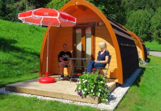 Hébergement glamping au Camping Putterersee : pods confortables en Autriche, terrasse, parasol rouge, deux personnes.