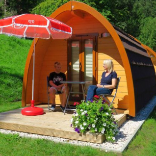 Glamping bij Camping Putterersee: gezellige pods in Oostenrijk, houten terras met parasol en twee mensen.