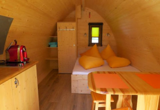 Indvendig billede af en glamping pod i træ med seng, bord, stole og kaffemaskine på Camping Putterersee.