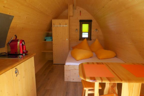 Interieur van een houten glamping pod bij Camping Putterersee met bed, tafel, krukken en koffiezetapparaat.