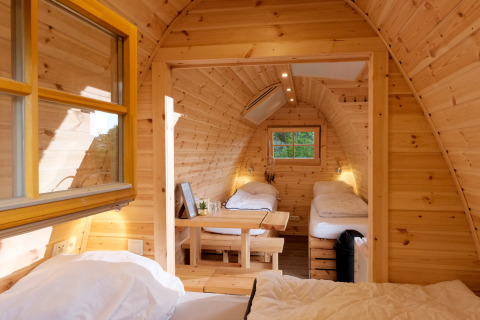 Cozy glamping pod interior with three single beds, natural wood paneling, and small windows for light.