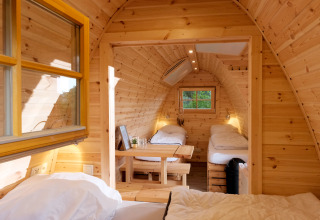 Indvendig udsigt til en hyggelig træhytte med tre enkeltstående senge og små vinduer i glampingstil.