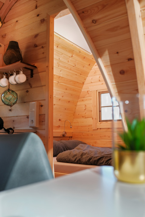 Interni di alloggio glamping in legno con zona notte compatta e finestra che illumina la stanza.