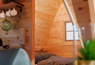 Gezellig houten glamping-interieur met kleine slaapnis en een raam met zicht op het buitenlicht.
