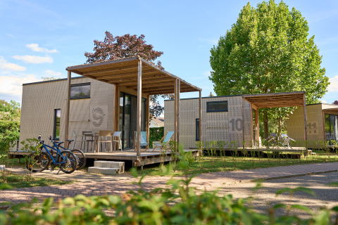 Tiny Houses en Strandcamping Podersdorf am See, Austria, con bicicletas y terrazas de madera bajo árboles verdes.