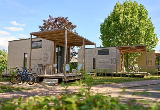 Tiny Houses en Strandcamping Podersdorf am See, Austria, con bicicletas y terrazas de madera bajo árboles verdes.