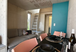 Modern glamping accommodation in a tiny wooden house with dining area, sofa and stairs, Podersdorf am See.