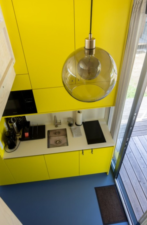 Pequeña cocina moderna con armarios amarillos y suelo azul en alojamiento glamping en Austria.