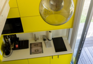 Pequeña cocina moderna con armarios amarillos y suelo azul en alojamiento glamping en Austria.