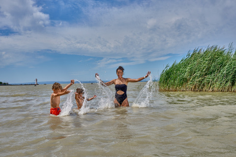 Family splashing water and laughing at Strandcamping Podersdorf am See - Tiny Houses, Austria, in summer.
