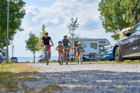 Familie fährt Fahrrad auf dem Campingplatz Strandcamping Podersdorf am See - Tiny Houses, Österreich, mit Wohnmobilen im Hintergrund.