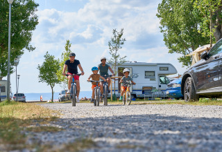 Familia en bicicleta en un camino de grava en Strandcamping Podersdorf am See - Tiny Houses, Austria, con autocaravanas de fondo.