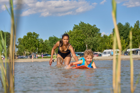Donna in costume nero gioca con bambino su tavola da surf allo Strandcamping Podersdorf am See, Austria.