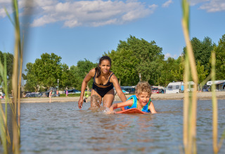 Woman in black swimsuit playing with boy on surfboard at Strandcamping Podersdorf am See, Austria.