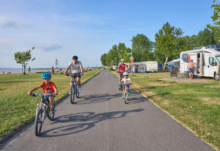 Family cycling on a path at Strandcamping Podersdorf am See - Tiny Houses, with RVs and the lake in the background.