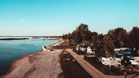Strandcamping Podersdorf am See avec tiny houses et caravanes au bord du lac, entouré d’arbres en Autriche.