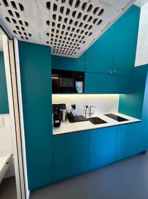 Modern kitchenette inside a Tiny House at Strandcamping Podersdorf am See with blue cabinets and appliances.