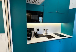 Modern kitchenette inside a Tiny House at Strandcamping Podersdorf am See with blue cabinets and appliances.