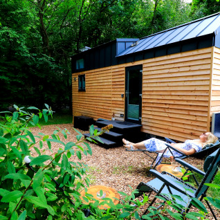 Kvinde slapper af udenfor et lille træhus omgivet af natur, Tinyhouse KLEINES EMS-IDYLL i Emsland.