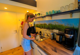 Vrouw bereidt een drankje in de keuken van Tinyhouse KLEINES EMS-IDYLL, een glampingverblijf in Emsland.
