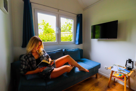 Mujer leyendo en un sofá azul en Tinyhouse KLEINES EMS-IDYLL, glamping acogedor en Emsland, Países Bajos.