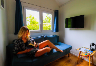 Mujer leyendo en un sofá azul en Tinyhouse KLEINES EMS-IDYLL, glamping acogedor en Emsland, Países Bajos.