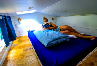 Donna che legge un libro su un letto accogliente nell’alloggio glamping Tinyhouse KLEINES EMS-IDYLL in Emsland.