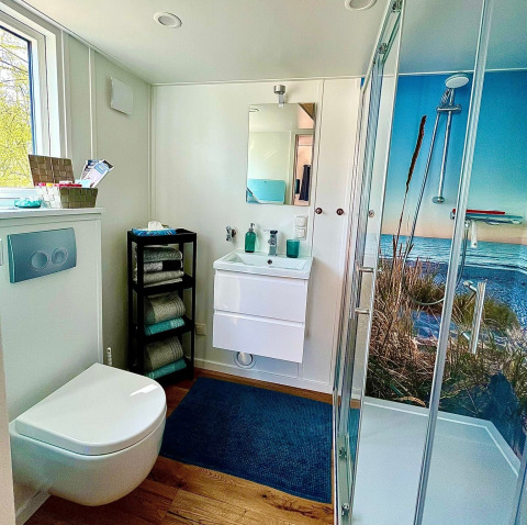 Baño moderno en Tinyhouse KLEINES EMS-IDYLL, Emsland, con ducha panorámica y toallas apiladas.