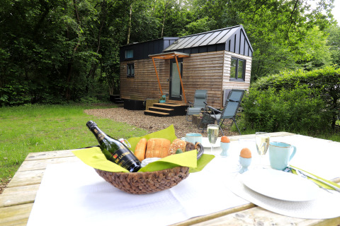 Glamping at Tinyhouse KLEINES EMS-IDYLL in Emsland, with outdoor breakfast table and woodland surroundings.