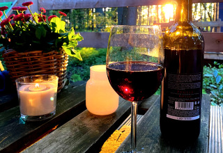 Wine, candles, and flowers on a wooden table at Tinyhouse KLEINES EMS-IDYLL glamping, sunset shining through trees.