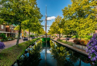 A boat in a scenic canal lined with trees and flowers, near Tinyhouse KLEINES EMS-IDYLL - Emsland camping.