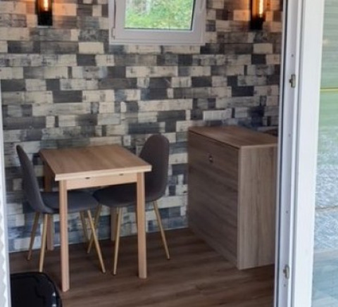 Vista interior de una casa tiny glamping con mesa, sillas y pared decorativa de madera en Mecklenburg-Vorpommern.