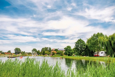 Vital CAMP Bayerbach glamping aan het water: luxe stacaravans tussen bomen, groen gras en blauwe lucht.