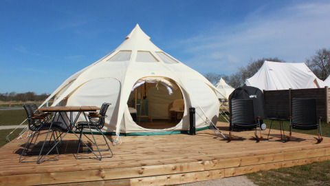 Tente de glamping à Marsk Camp au Danemark avec terrasse en bois, chaises extérieures et environnement naturel.