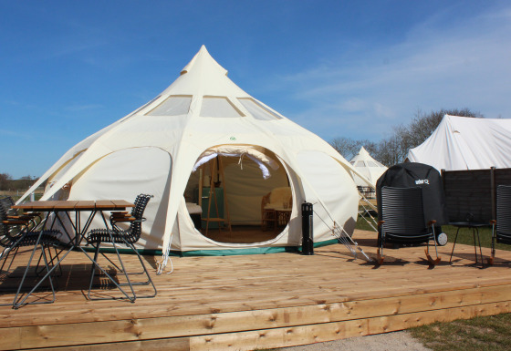 Glampingtent bij Marsk Camp in Denemarken met houten terras, buitenstoelen, tafel en groene omgeving.
