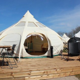 Tenda glamping al Marsk Camp in Danimarca, con terrazza in legno, sedie, tavolo e ambiente naturale.