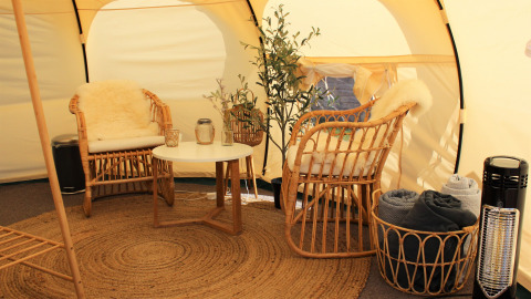 Intérieur d'une tente glamping Marsk Camp au Danemark avec fauteuils en osier et décoration confortable.