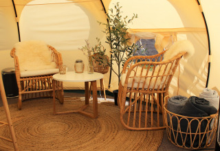 Interior de tienda glamping en Marsk Camp Glampingtenten Dinamarca, con sillas de mimbre y decoración acogedora.