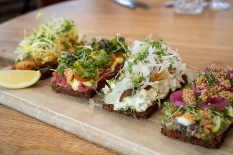 Assortiment de smørrebrød danois avec garnitures fraîches et herbes, présenté sur une planche en bois.