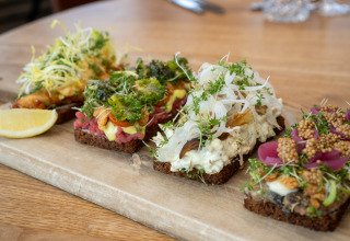 Et udvalg af danske smørrebrød med forskelligt pålæg og friske krydderurter, serveret på træplade.