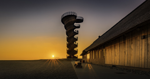 Marsk Camp Glampingzelte in Dänemark, ein spiralförmiger Aussichtsturm bei Sonnenuntergang und Holzgebäude.